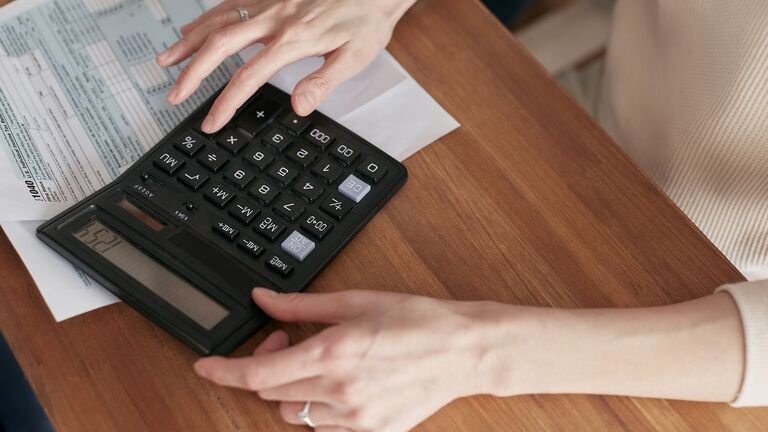 Manos que hacen cuentas con una calculadora sobre una mesa de madera antes de contratar un guardamuebles