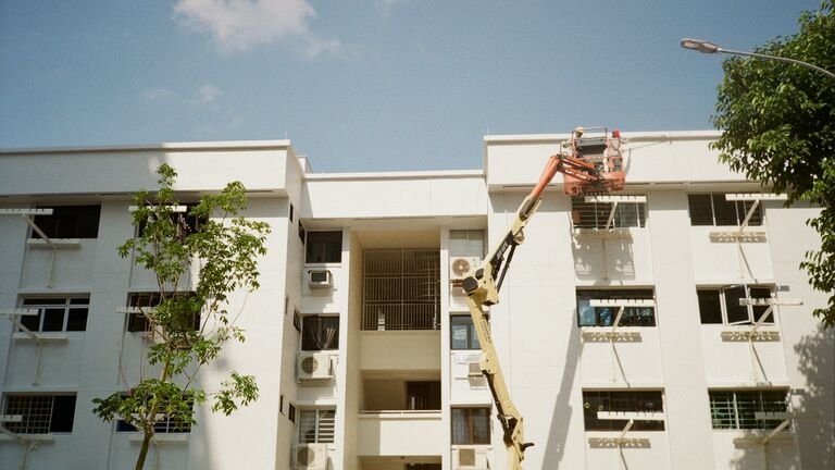 Plataforma elevadora con brazo articulado trabajando junto a la fachada de un bloque de pisos
