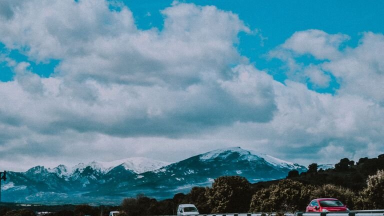 Furgoneta blanca circulando por una autovía de meseta con una sierra nevada al fondo y cielo con nubes