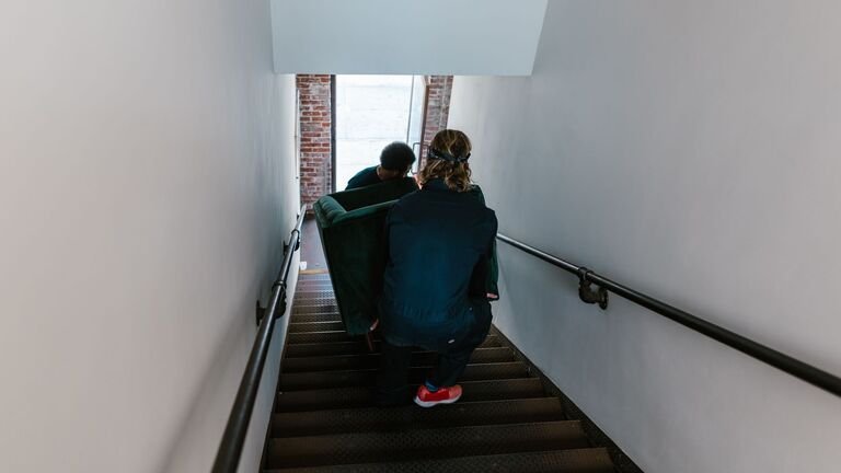 Dos operarios bajan un sillón por la escalera estrecha de un edificio sin ascensor durante una mudanza